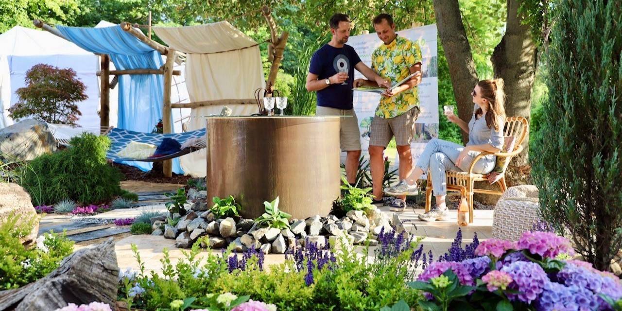 Drei Menschen in Beratungsgespräch auf Terrasse im Garten mit Hängematte und Wasserfalltisch